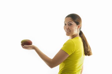 Side view of a happy looking young woman holding a delicious mango on a light background. Healthy food and lifestyle concept.の写真素材
