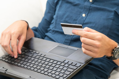 Close up of a man holding a credit card while using a laptop. Commerce and payment concept.