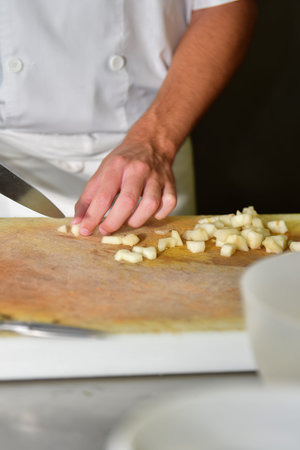 Male chef cutting potatoes with a kitchen knife on a cutting board on an out of focus background. Cooking concept.の写真素材
