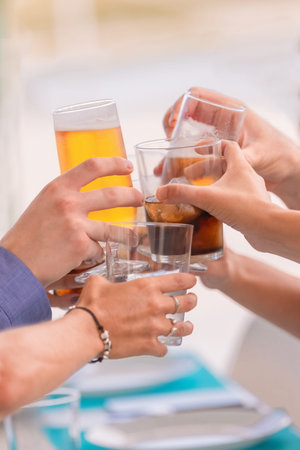 Close up of an assortment of hands doing a toast with different drinks on an out of focus...