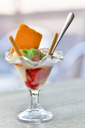Close up of a delicious looking ice cream cup with crispy wafer sticks and a spoon on a table on an...