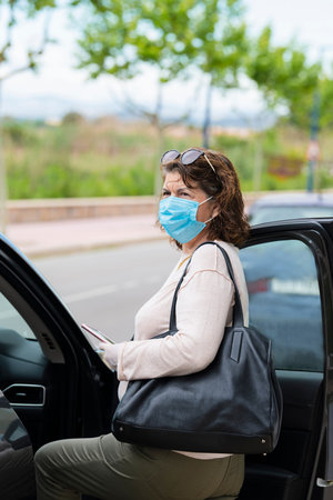 a woman with protective mask and gloves enters of his car. Infection prevention and control of...