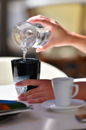 Close up of female hands pouring water from a jar into a cup on an out of focus background....