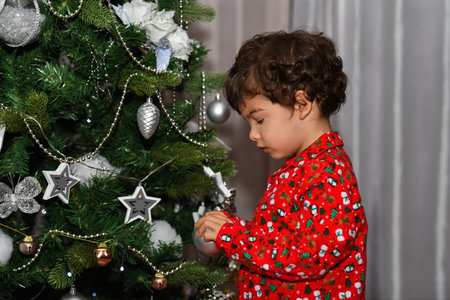 Curious male child touching an ornament in a Christmas tree on an out of focus background. Christmas holiday and childhood concept.の写真素材