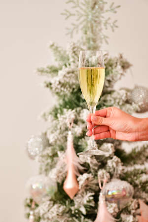 A female hand holding a champagne glass with an out of focus Christmas tree and traditional sweets at the back. Christmas celebration concept.の写真素材