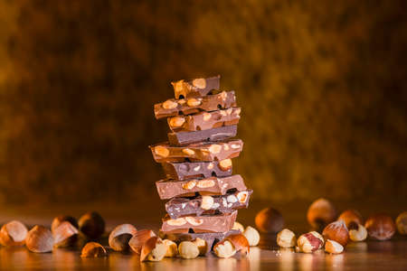 Closeup of assorted chocolate chunks with hazelnuts and almonds stacked forming a tower surrounded by hazelnuts on an out of focus background.の写真素材