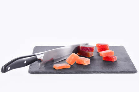 Close up of a delicious looking bits of fruit paste and a kitchen knife on a dark plate on a light background. Traditional sweets concept.の写真素材