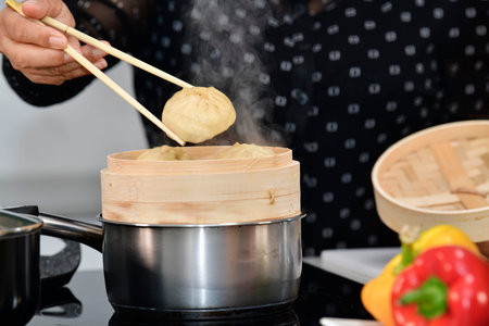 Close up of a dumpling being put into a traditional chinese bamboo steamer on an out of focus...
