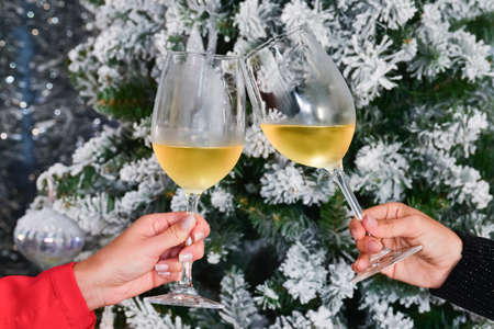 Close up of a toast being made by two female hands and two glasses of wine on an out of focus Christmas background. Christmas and celebration concept.の写真素材