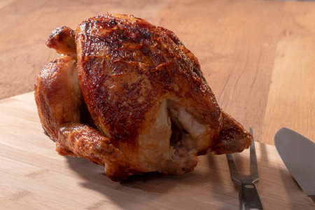 Select focus of a tempting rotisserie chicken with a carving fork and a knife on a cutting boardの写真素材