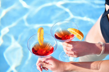 Close up of two delicious looking cocktails being held by female hands on an out of focus...