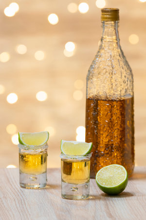 Shots of tequila with lime slices and an out of focus bottle at the back