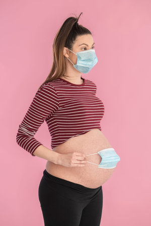 Pregnant woman wearing mask holding a mask on her belly