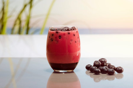 a glass of fruit juice with blueberries next to some more blueberriesの写真素材