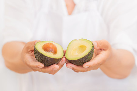 Hands holding a fresh avocado cut in half: Selective focus and close up. Healthy food concept.