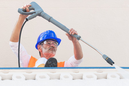 Mature worker with safety gear using a pressure washer