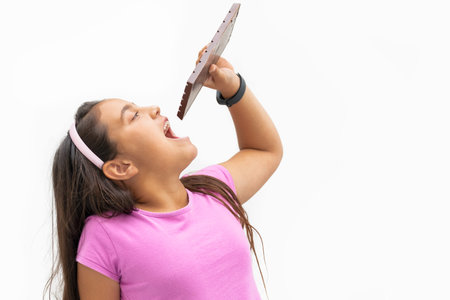 Happy little girl holding a chocolate bar over her open mouth: Selective focus and close up....