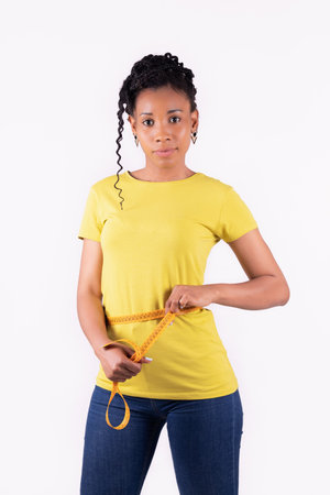 Happy looking afro american woman measuring her waistの写真素材