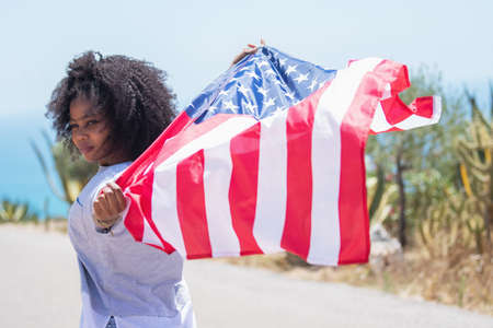 Afro american girl waving an american flag on a roadの写真素材