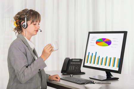 Side view of woman customer support call operator in office with statistics and charts on screen of...