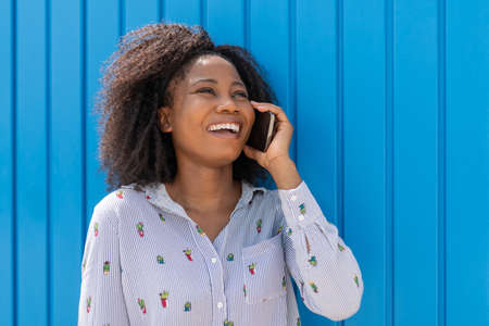 Young african woman smiling and using mobile phoneの写真素材