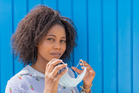 African American woman looking at camera holding face mask about to put it on her face