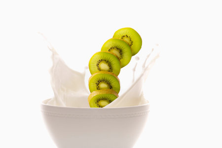 Kiwi slices falling into a bowl of milkの写真素材