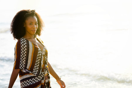 African woman smiling walking along the beach and looking at camera