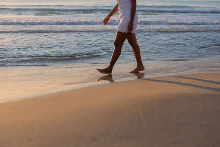 Cropped view of the legs of an anonymous woman walking along the beach at sunsetの写真素材