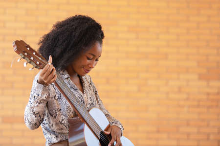 Cropped view of a young woman playing guitar looking down on a brick wall backgroundの写真素材
