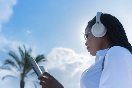 Focused african woman wearing headphones reading a bookの写真素材