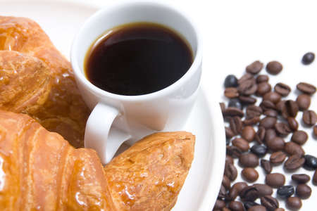 Forefront of a cup of coffee with croissants and coffee beans backgroundの写真素材