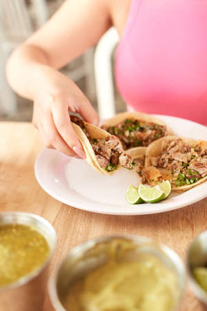 Girl eating delicious taco with salsa and a variety of toppings. Mexican taco with sauce, taco al pastor.の写真素材