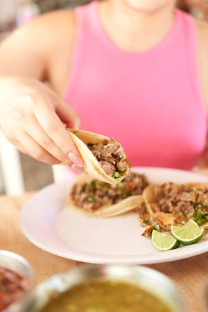 Girl eating delicious taco with salsa and a variety of toppings. Mexican taco with sauce, taco al pastor.の写真素材