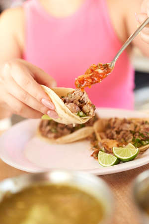 Girl eating delicious taco with salsa and a variety of toppings. Mexican taco with sauce, taco al pastor.の写真素材