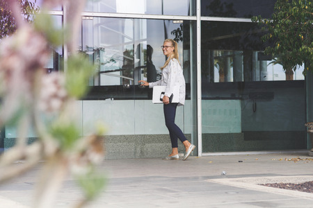 Young woman holding a white laptop entering a buildingの写真素材