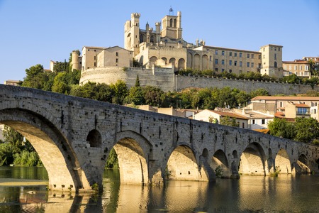 Views at sunset of the French city of Beziers, with trees and the old bridge reflected over the river Orb, and the 13th-century Cathedral of Saint Nazaire in the backgroundのeditorial素材