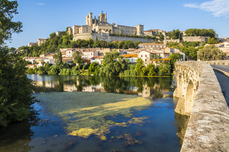 Views at sunset of the French city of Beziers, with trees, the river Orb, and the 13th-century Cathedral of Saint Nazaire in the backgroundの写真素材