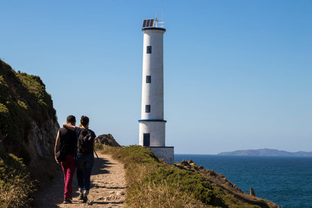A couple walks to the iconic white lighthouse at Cabo Home, Cangas, Galicia, Spainの写真素材