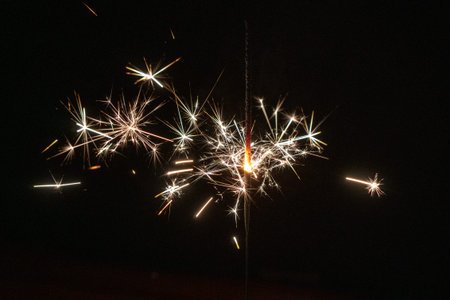 Sparkler burns down against a dark background and sends sparks into the environment. Solemnly.