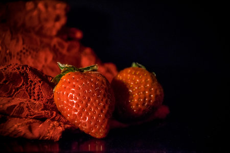 Two strawberries and red lace on a black backgroundの写真素材