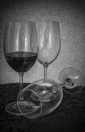 Black and white photo of three glasses of wine on a table, one full and two emptyの写真素材