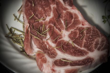 Raw pork meat ready for cooking and rosemary on a tableの写真素材