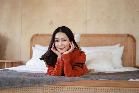 Portrait of a beautiful Asian woman with healthy skin. She was wearing a sweater. She smiled happily and looking at the camera on the bed. Winter healthの写真素材