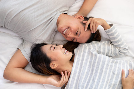 The Close-up of the happy an Asian couple is lying in bed together. They meet each other's eyes showing love.の写真素材