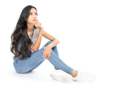 A young Asian woman wore a casual dress sit on the floor. She looks at the copy space on the top....