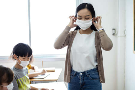 An Asian female teacher was wearing a face mask while teaching students in the classroom. Group of Diversity students wear a protective face mask to prevent the spread of the Coronavirus. The new normal concept in schoolの写真素材