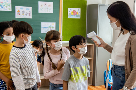 A group of Children students wearing masks lined up waiting for woman teachers to Check Fever by...