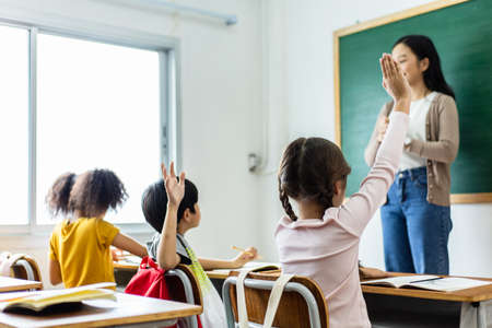 Diversity of elementary school students raise their hands to answer teacher questions. Back to school conceptの写真素材