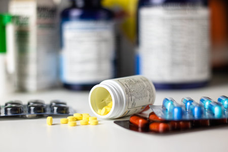 yellow prescription pills spilled onto a table with many prescription bottles in the background.